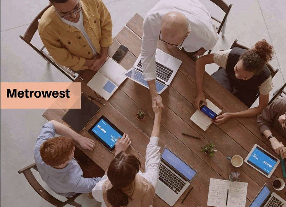 An overhead view of a property management team shaking hands across a wooden table with laptops and tablets, featuring a Metrowest logo banner.